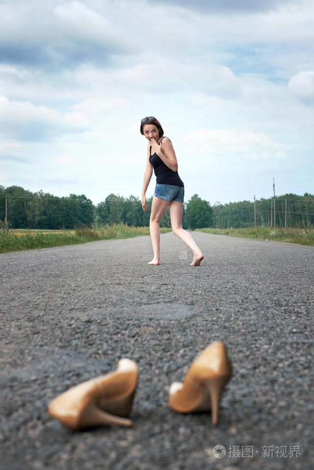 年轻的女孩赤脚走在路上她把鞋子落在路上忘记了夏天和旅行的概念